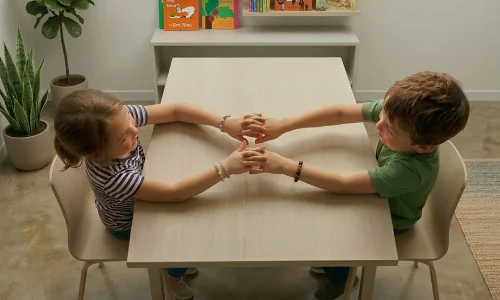 zwei kinder halten sich die hände am tisch bei der gruppentherapie